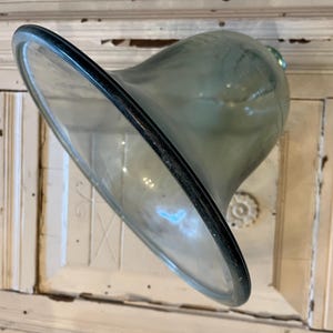 May include: A clear, flared glass vase with a dark rim. The vase has a wide, open top and a rounded body. The glass has a slight green tint. The vase is likely used for decorative purposes.