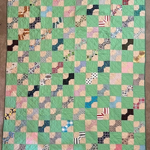 May include: A rectangular quilt featuring a grid pattern of light green squares alternating with beige squares. The beige squares contain various multi-colored fabric patches in diverse patterns, including stripes, polka dots, and floral prints.
