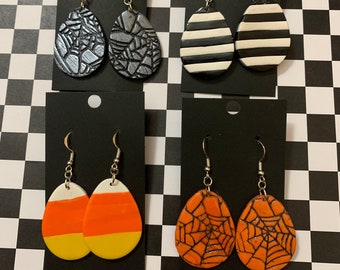 May include: Four pairs of Halloween-themed dangle earrings. The earrings are made of polymer clay and feature a variety of designs, including candy corn, spiderwebs, and stripes.