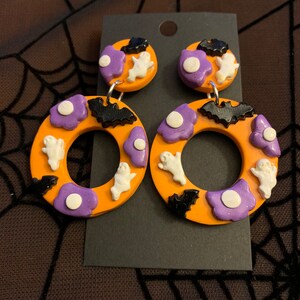 May include: Orange and purple Halloween themed dangle earrings with ghosts, bats, and white dots.