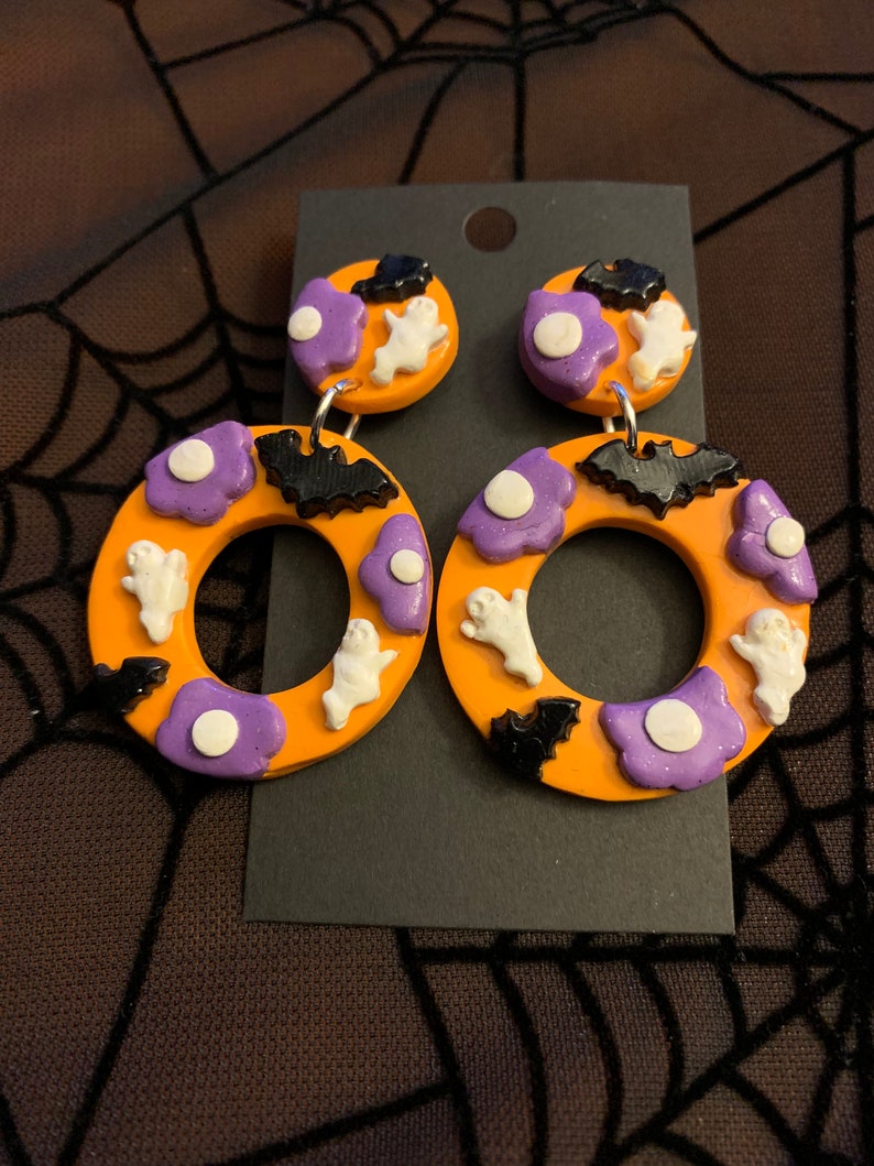 May include: Orange and purple Halloween themed dangle earrings with ghosts, bats, and white dots.