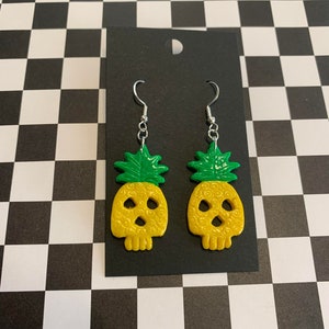 May include: A pair of yellow and green pineapple skull earrings with silver hooks.