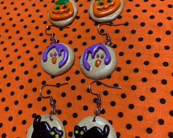 Könnte beinhalten: Ein Set mit sechs Halloween-Ohrringen. Die Ohrringe sind aus Polymer Clay gefertigt und zeigen einen Kürbis, ein Gespenst und eine schwarze Katze. Die Ohrringe sind alle an silbernen Haken.