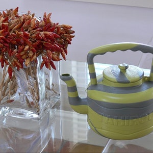 May include: A yellow and gray striped teapot with a handle and a lid. The teapot has the word "TAHIFOU" written on the side.