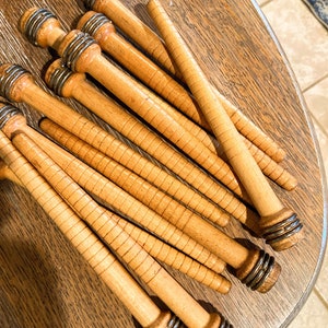 May include: A group of wooden spools with metal rings at the ends. The spools are stacked on top of each other and are arranged in a fan shape. The spools are a light brown color and have a smooth, polished finish.