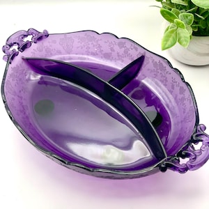 May include: A vintage, oval-shaped divided serving dish in a deep purple hue. The dish features a floral pattern etched into the glass and is divided into three sections. It has ornate handles on each end, adding to its classic design.