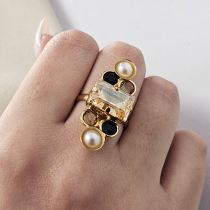 May include: Gold ring with a large rectangular clear stone surrounded by smaller black and white stones.