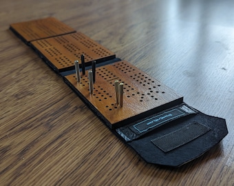 May include: A wooden cribbage board with a black leather carrying case. The board is folded up and has pegs inserted into the holes. The case has a velcro closure and the text "DrunkenSailor.com" printed on the flap.