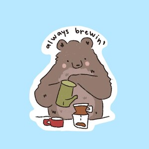 May include: A sticker featuring a cartoon bear brewing coffee. The bear is brown with a green coffee pot and a red mug. The text "always brewin'" is above the bear. The background is light blue.