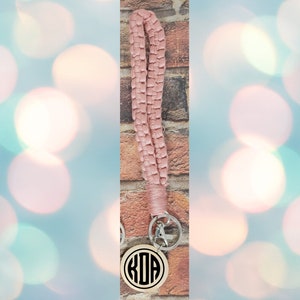 May include: A pink braided lanyard with a silver key ring and a round wooden keychain with the monogram "KDA" in black.