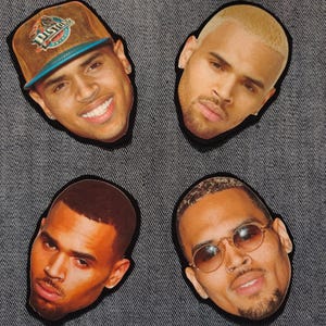 May include: Four die-cut stickers featuring the face of a celebrity. One sticker shows the celebrity wearing a brown and blue baseball cap. The other stickers show the celebrity with different hairstyles and facial hair.