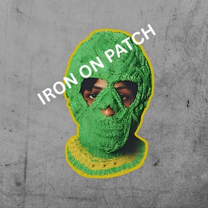 May include: A green knitted balaclava with yellow trim, set against a gray background. The text "IRON ON PATCH" is printed across the top of the image. The balaclava covers the head and face, with openings for the eyes and nose.