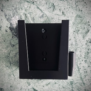 May include: Black wall mount with a rectangular opening for a device and a small side compartment.
