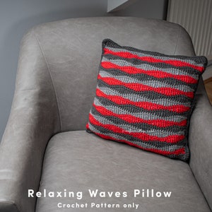 May include: A red and grey crocheted cushion with a wave pattern. The cushion is on a grey sofa. Relaxing Waves Pillow Crochet Pattern only.
