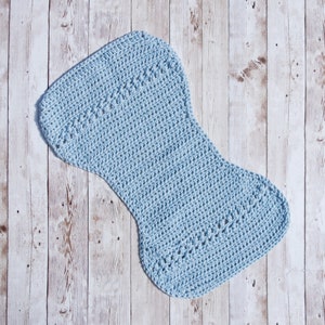 May include: A light blue crocheted baby blanket in the shape of a  foot. The blanket is lying on a light wood background.