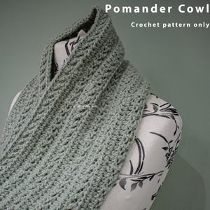 May include: A sage green crocheted cowl, a type of neck warmer, is draped over a white mannequin with a floral pattern. The text "Pomander Cowl Crochet pattern only" is visible at the top of the image.