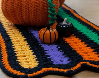 May include: A crocheted rug with black, orange, yellow, green and purple stripes. There are three small crocheted pumpkins on the rug, two orange and one black.