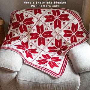 Puede incluir: Una manta de crochet de copo de nieve roja y blanca con un borde. La manta est&aacute; doblada y drapeada sobre una silla. El texto "Nordic Snowflake Blanket PDF Pattern only" es visible en la parte superior de la imagen.