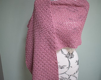 May include: A pink crochet wrap, draped over a white mannequin with floral pattern. The wrap is made with a delicate open stitch pattern.