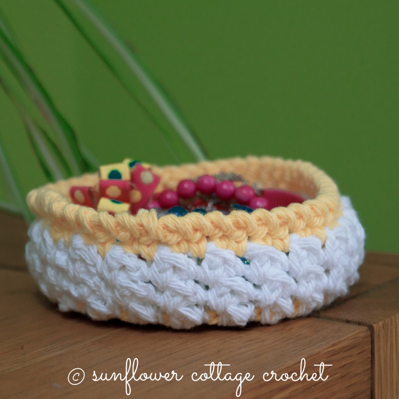 May include: A white and yellow crocheted basket with a pink and green polka dot ribbon and pink beads inside.  &copy; sunflower cottage crochet