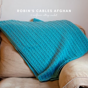 May include: A teal blue crocheted blanket with a cable stitch pattern, draped over a tan couch. The text "ROBIN'S CABLES AFGHAN @sunflower cottage crochet" is visible in the top center of the image.