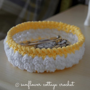 May include: A crocheted bowl with a white and yellow striped design. The bowl is filled with a watch and a silver pin.