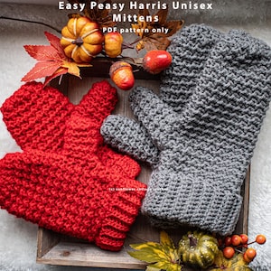 May include: A pair of red and gray crocheted mittens with a textured stitch pattern. The mittens are displayed on a wooden tray with fall-themed decorations, including pumpkins and acorns. The text "Easy Peasy Harris Unisex Mittens PDF pattern only" is visible at the top of the image.