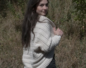 May include: A white crocheted cardigan with a loose fit and a slightly open front. The cardigan is worn over a black skirt.