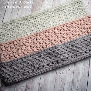 Könnte beinhalten: Ein gehäkeltes Kragenschal mit drei Streifen in verschiedenen Farben: hellgrau, rosa und grau. Der Kragenschal ist mit einem strukturierten Stichmuster gearbeitet. Der Text "Emilia Cowl Pattern PDF Only" ist in der oberen linken Ecke des Bildes sichtbar.