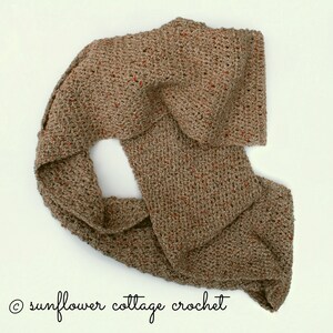 May include: A brown crocheted scarf with flecks of red throughout. The scarf is folded and draped over itself.