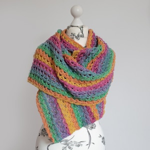 May include: A colorful crochet shawl with a striped pattern in shades of green, purple, orange, and pink. The shawl is draped over a white mannequin.