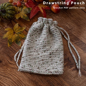 May include: A beige crocheted drawstring pouch with a brown and green speckled pattern. The pouch is on a wooden surface.