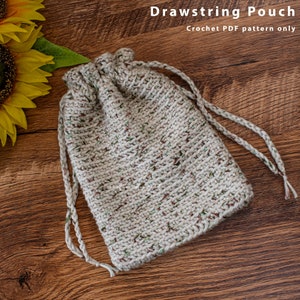 May include: A crocheted drawstring pouch with a beige and brown speckled yarn. The pouch is lying on a wooden surface.