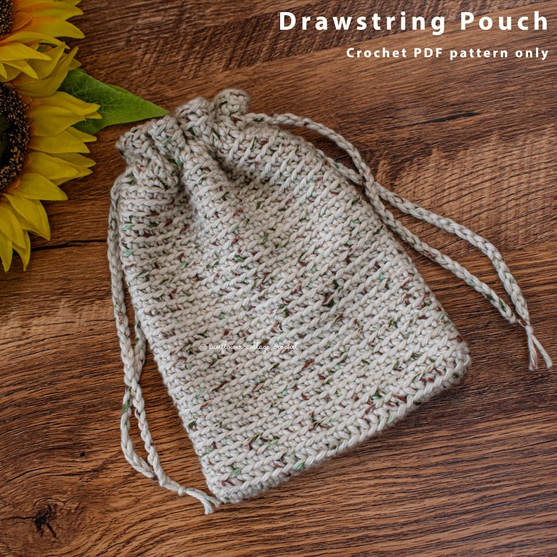 May include: A crocheted drawstring pouch with a beige and brown speckled yarn. The pouch is lying on a wooden surface.