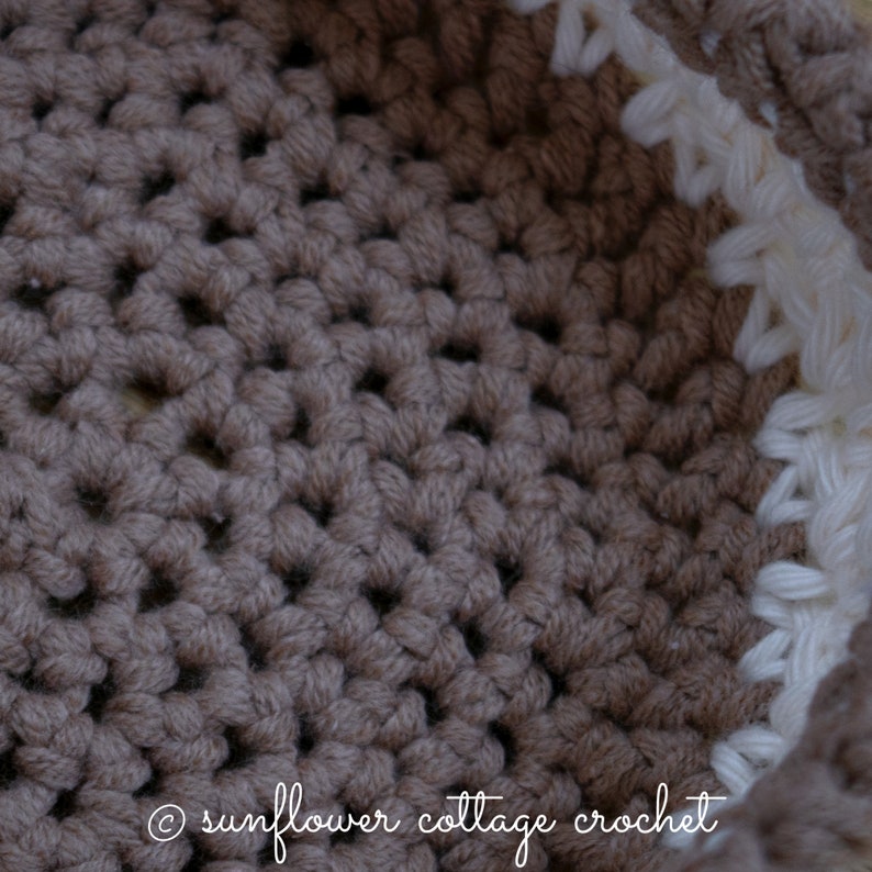 May include: Close-up of a brown crocheted basket with a white crocheted border. The basket is made with a simple stitch pattern and has a textured look. The text "sunflower cottage crochet" is visible at the bottom of the image.