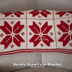 Puede incluir: Una manta de punto de nieve n&oacute;rdica de color blanco y rojo con un borde de rayas rojas y blancas. La manta est&aacute; doblada y drapeada sobre un sof&aacute;. El texto "Nordic Snowflake Blanket PDF Pattern only" est&aacute; impreso debajo de la manta.