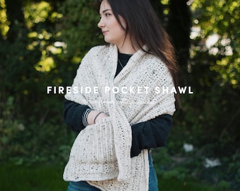 May include: A white crochet shawl with a large pocket. The shawl is worn by a person standing in front of a green background.