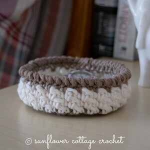 May include: A crocheted bowl with a brown and white striped pattern. The bowl is made with a thick yarn and has a slightly rounded shape.