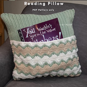 May include: A green crocheted pillow with a pocket for a book. The pocket is lined with a beige and white chevron pattern.