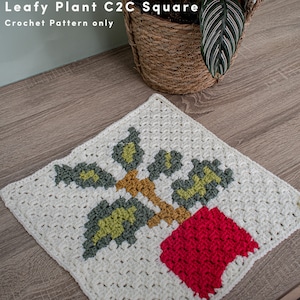 May include: A crocheted square featuring a leafy plant in a red pot. The plant is made with green, yellow, and brown yarn. The square is made with white yarn.
