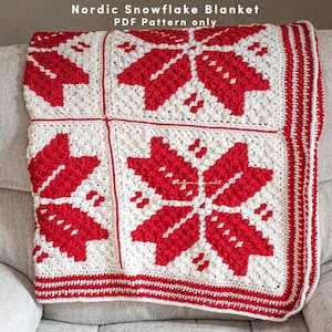 Puede incluir: Una manta de crochet blanca y roja con un patr&oacute;n de copo de nieve. La manta est&aacute; doblada y sentada en un sof&aacute;. El texto "Nordic Snowflake Blanket PDF Pattern only" est&aacute; en la parte superior de la imagen.