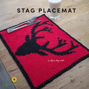 Puede incluir: Un mantel individual de crochet rojo con una silueta de ciervo negra en el centro. El mantel individual tiene un borde negro. El texto "STAG PLACEMAT" está en la parte superior de la imagen. El texto "sunflower cottage crochet" está en la parte inferior de la imagen.