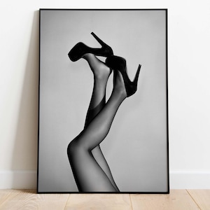 Könnte beinhalten: Schwarz-Weiß-Druck in einem Rahmen, der Beine in schwarzen Strümpfen und High Heels zeigt. Die Beine sind nach oben gerichtet, die Absätze zeigen nach oben. Das Bild verwendet Schatten und Kontraste, um einen auffälligen visuellen Effekt zu erzeugen.