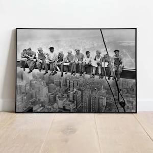 Könnte beinhalten: Schwarzweißfoto einer Gruppe von Bauarbeitern, die auf einem Stahlträger hoch über der Stadt sitzen. Die Arbeiter essen zu Mittag und schauen auf die Stadtlandschaft. Das Foto ist ein klassisches Bild der amerikanischen Arbeit und des Baus von Wolkenkratzern.