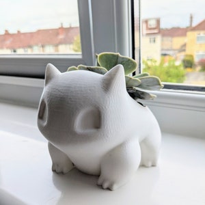 May include: A white ceramic planter shaped like a Pokemon character, with a small succulent plant growing out of the top.