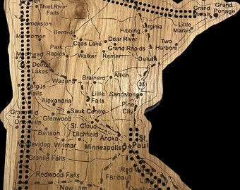 May include: A wooden map of Minnesota showing the names of cities and towns across the state. The map is a light brown colour and has a distressed look. The map is surrounded by a dark brown border.