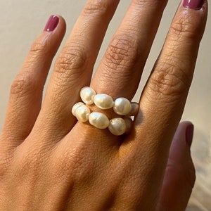 Könnte beinhalten: Ein Ring mit einer doppelten Reihe weißer Perlen. Der Ring wird an einem Finger getragen.