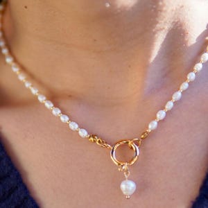 Könnte beinhalten: Eine goldene Kettenkette mit einem Perlenanhänger und einem Toggle-Verschluss. Die Kette besteht aus kleinen weißen Perlen und goldenen Perlen.