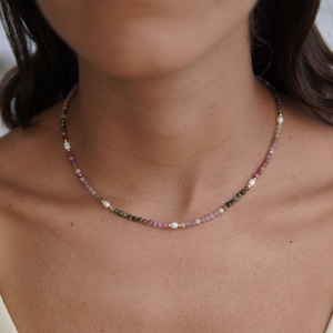 May include: A delicate necklace featuring small pink, green and brown beads with white pearl accents.