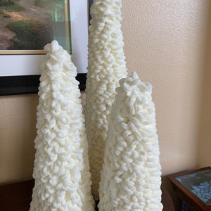 May include: Three white yarn Christmas trees of varying sizes. The trees are cone-shaped and made of fluffy yarn.